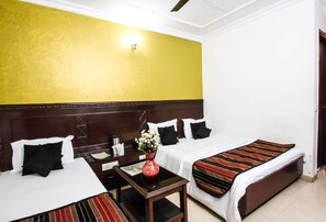 A hotel room with two beds, a nightstand, a vase with flowers, and a wall-mounted light fixture. - Hotel Pallvi Palace (New Delhi)