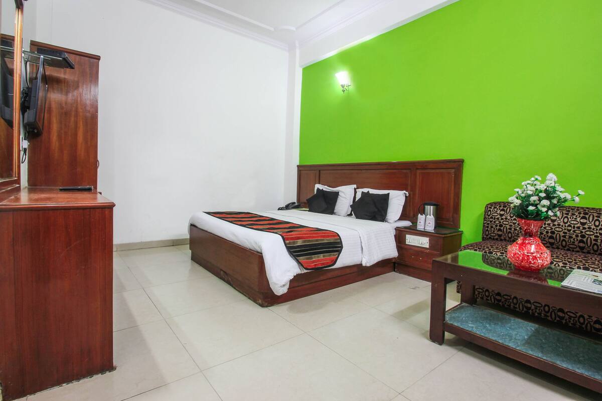 A hotel room with a bed, a wooden desk, a green accent wall, and a sofa.