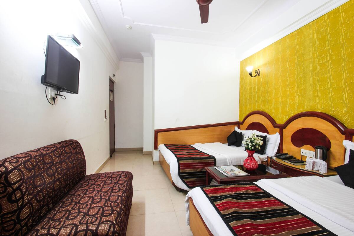 A hotel room with two beds, a sofa, a TV, and a yellow accent wall.