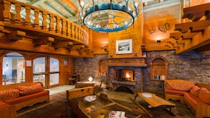A cozy lodge interior with a stone fireplace, wooden furnishings, and a balcony with a railing. - Residence  Le Cristal d'Argentière (Chamonix-Mont-Blanc)