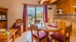 A cozy dining area with a wooden table and chairs, a view of mountains through a glass door, and a kitchen with wooden cabinets. - Residence  Le Cristal d'Argentière (Chamonix-Mont-Blanc)