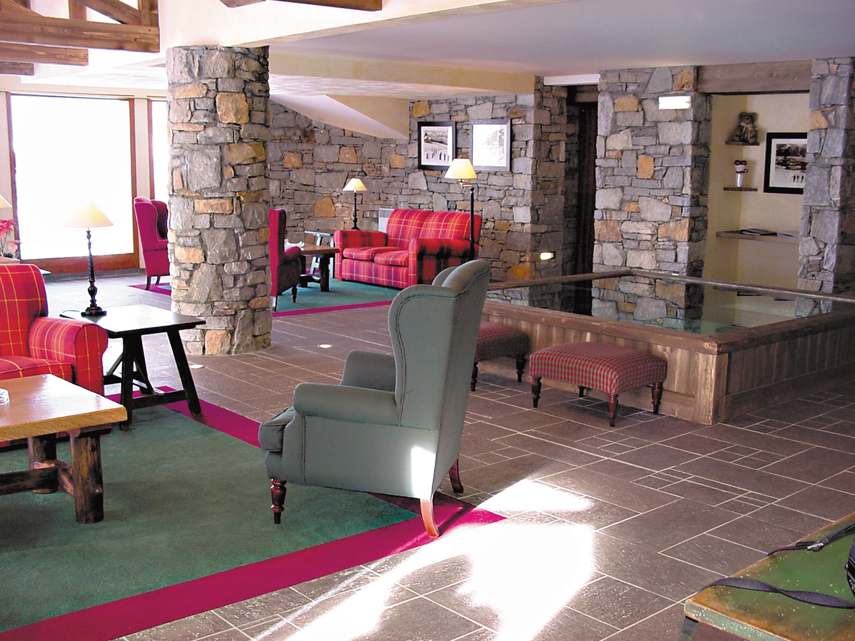 A lobby with stone walls, red and grey upholstered seating, a glass railing, and a green carpet.