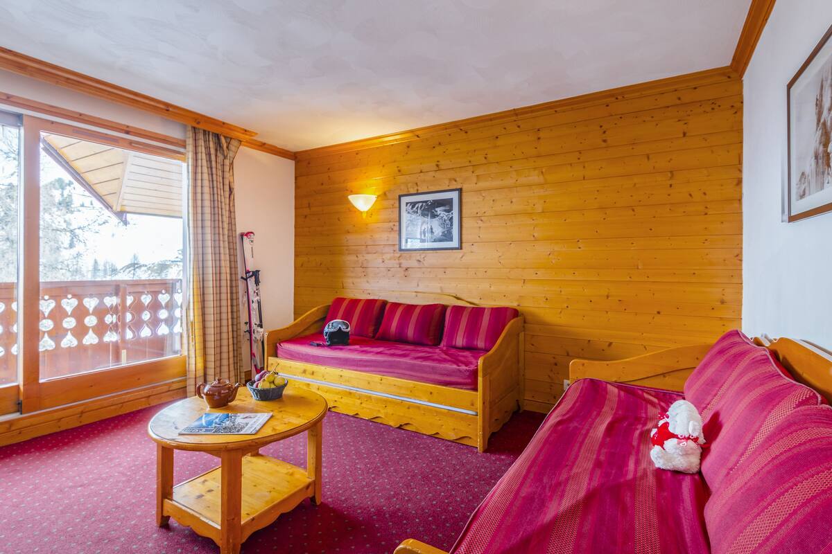 Une pièce chaleureuse avec un décor intérieur en bois, un canapé, une table et une fenêtre donnant sur un beau paysage.