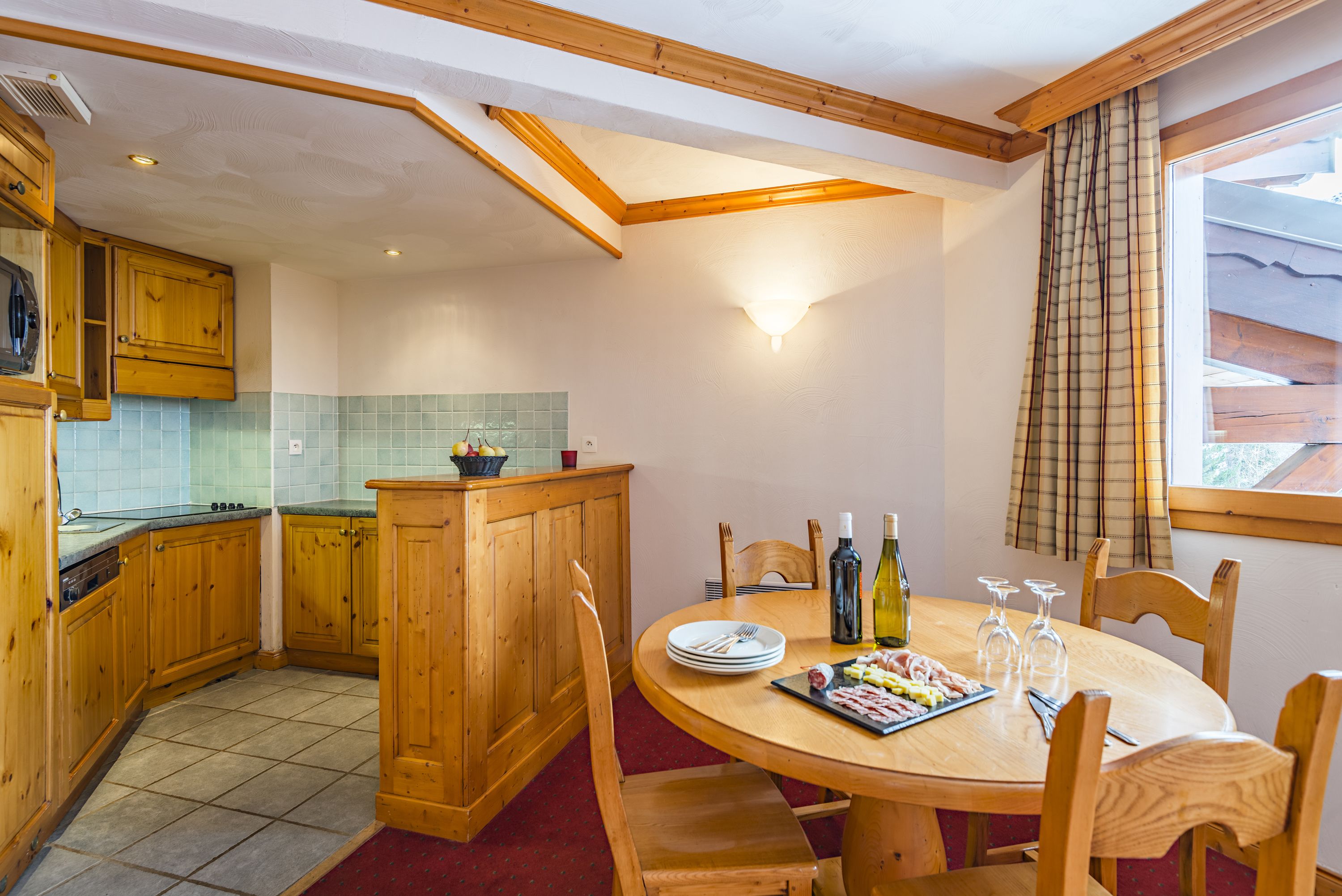 A kitchen with wooden cabinets, a dining table with chairs, and a window with curtains.