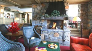 A cozy living room with a stone fireplace, plaid furniture, and a Christmas tree. - Résidence Lagrange Vacances Aspen (La Plagne-Tarentaise)