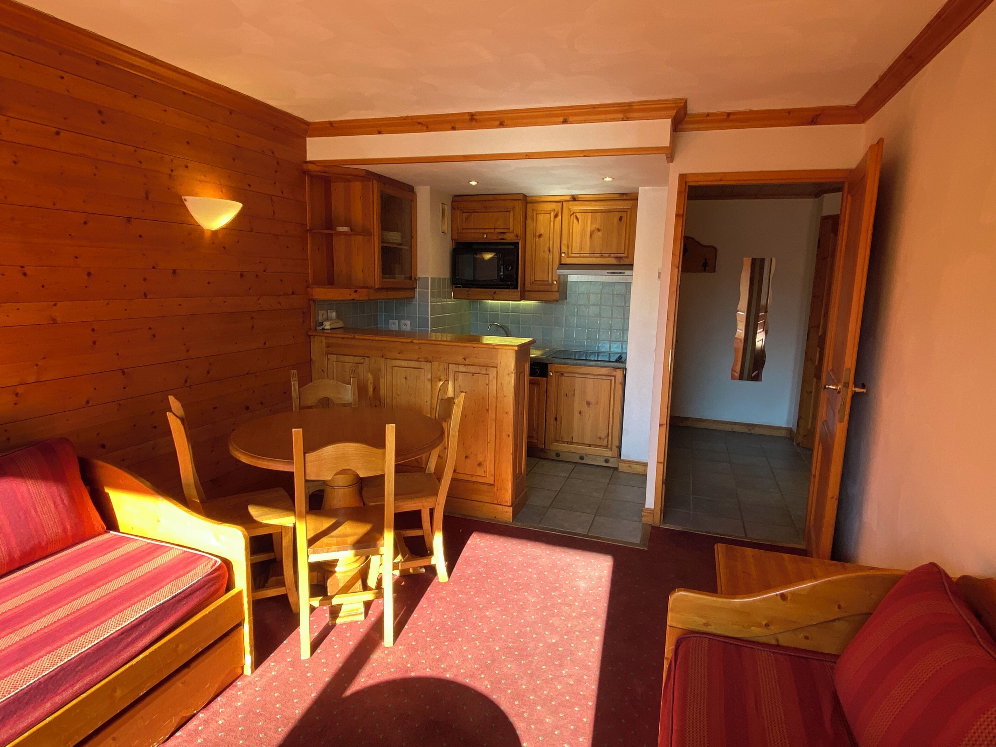 A cozy cabin interior with a dining area, wooden furniture, and a kitchen with wooden cabinets and a refrigerator.
