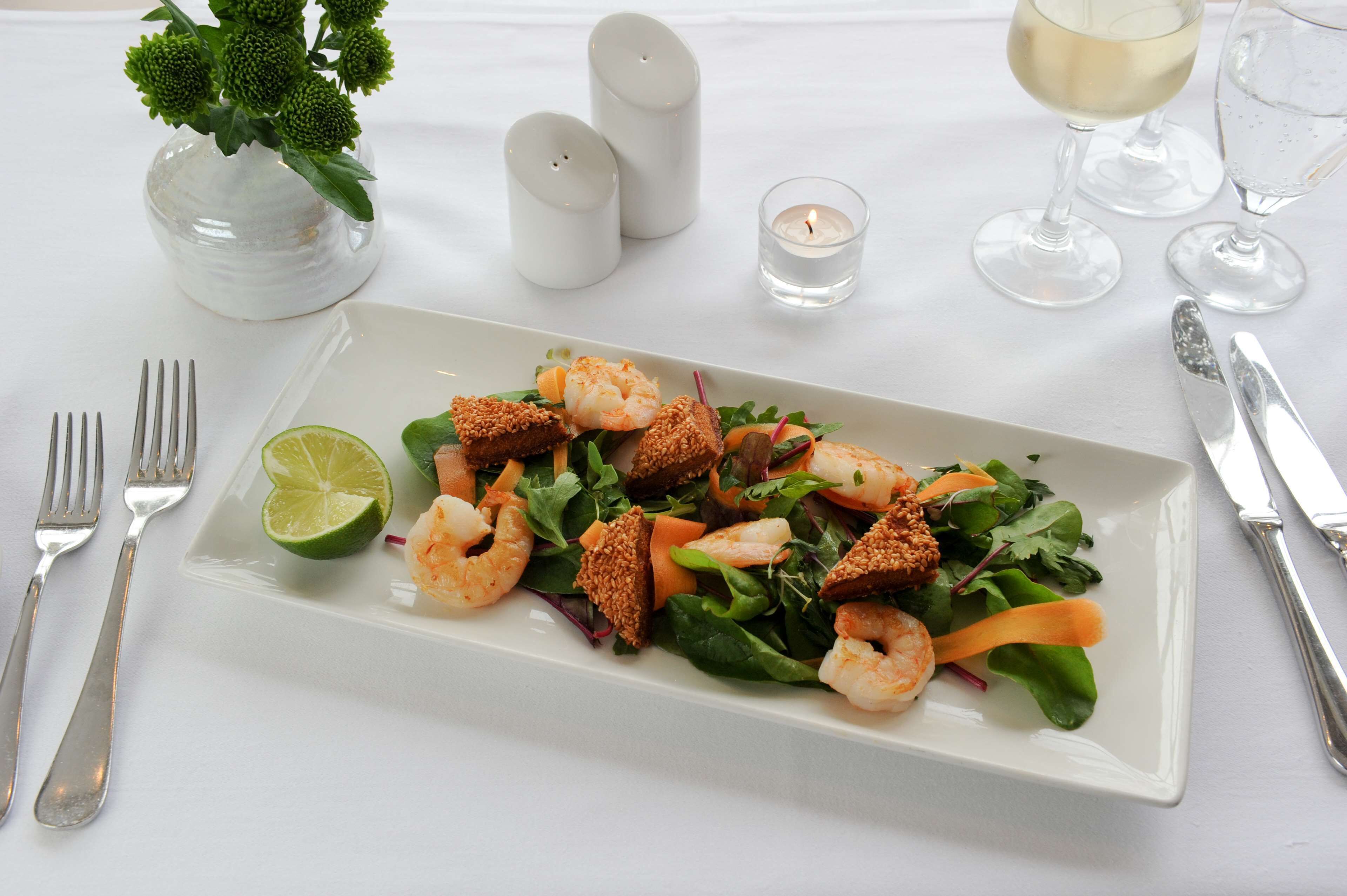 A rectangular white plate with a seafood salad, including shrimp and greens, accompanied by a lime wedge.