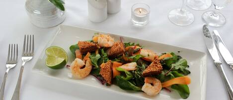 A rectangular white plate with a seafood salad, including shrimp and greens, accompanied by a lime wedge.