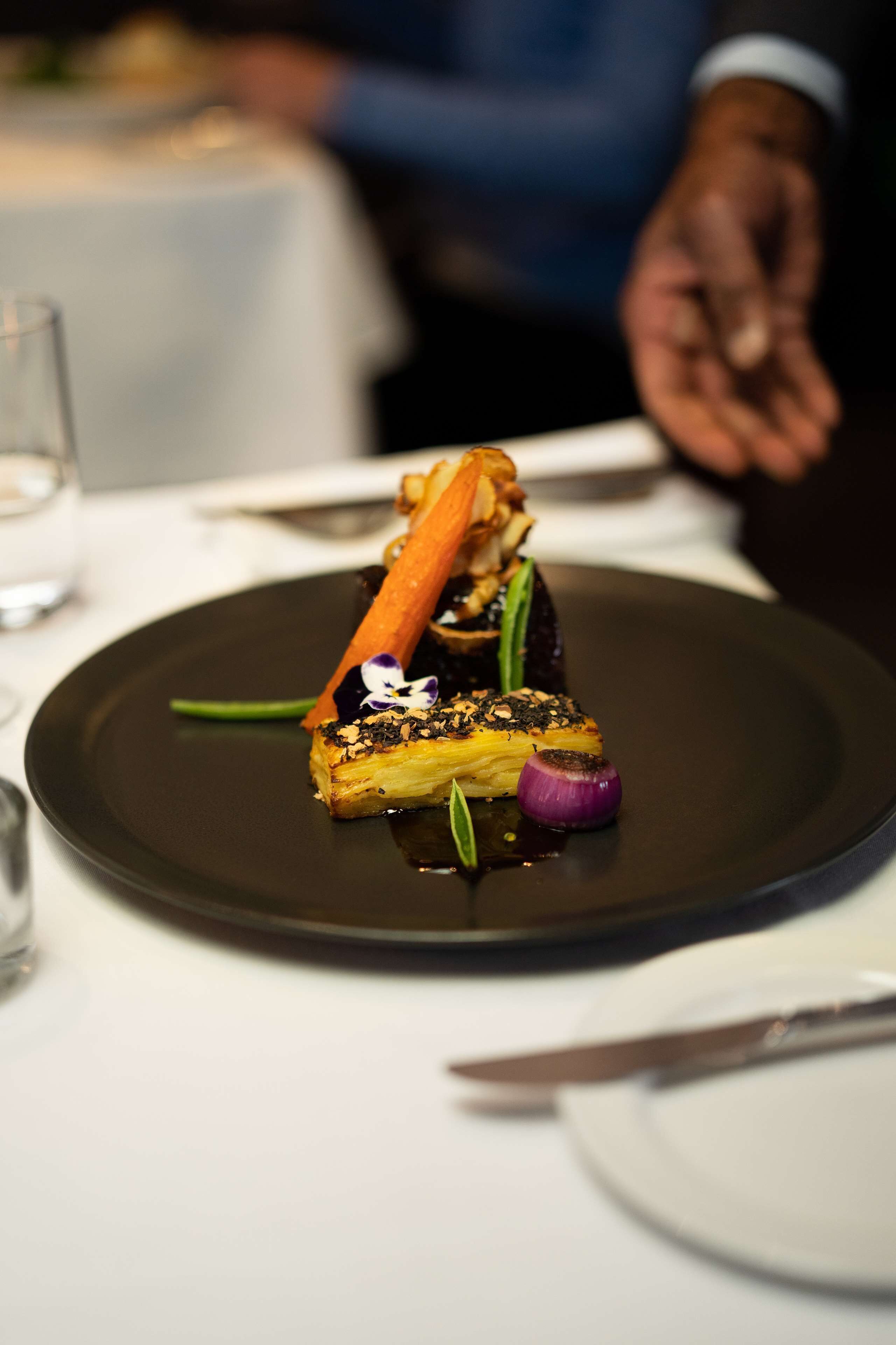 Un plato de comida con un fondo oscuro, un trozo de carne, una zanahoria y algunas verduras.