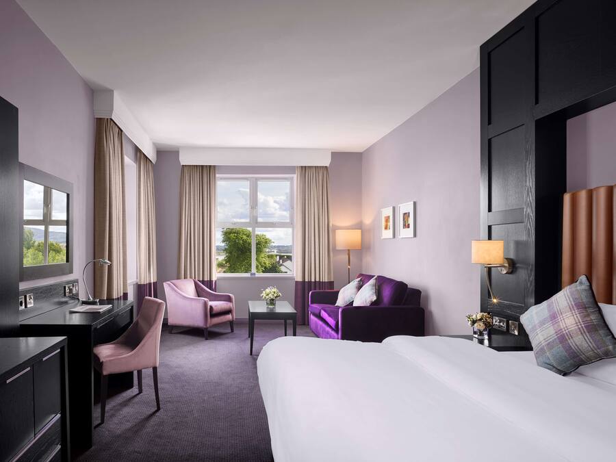 Habitación de hotel con cama, escritorio, sillón, sofá y ventana con vista a la vegetación.