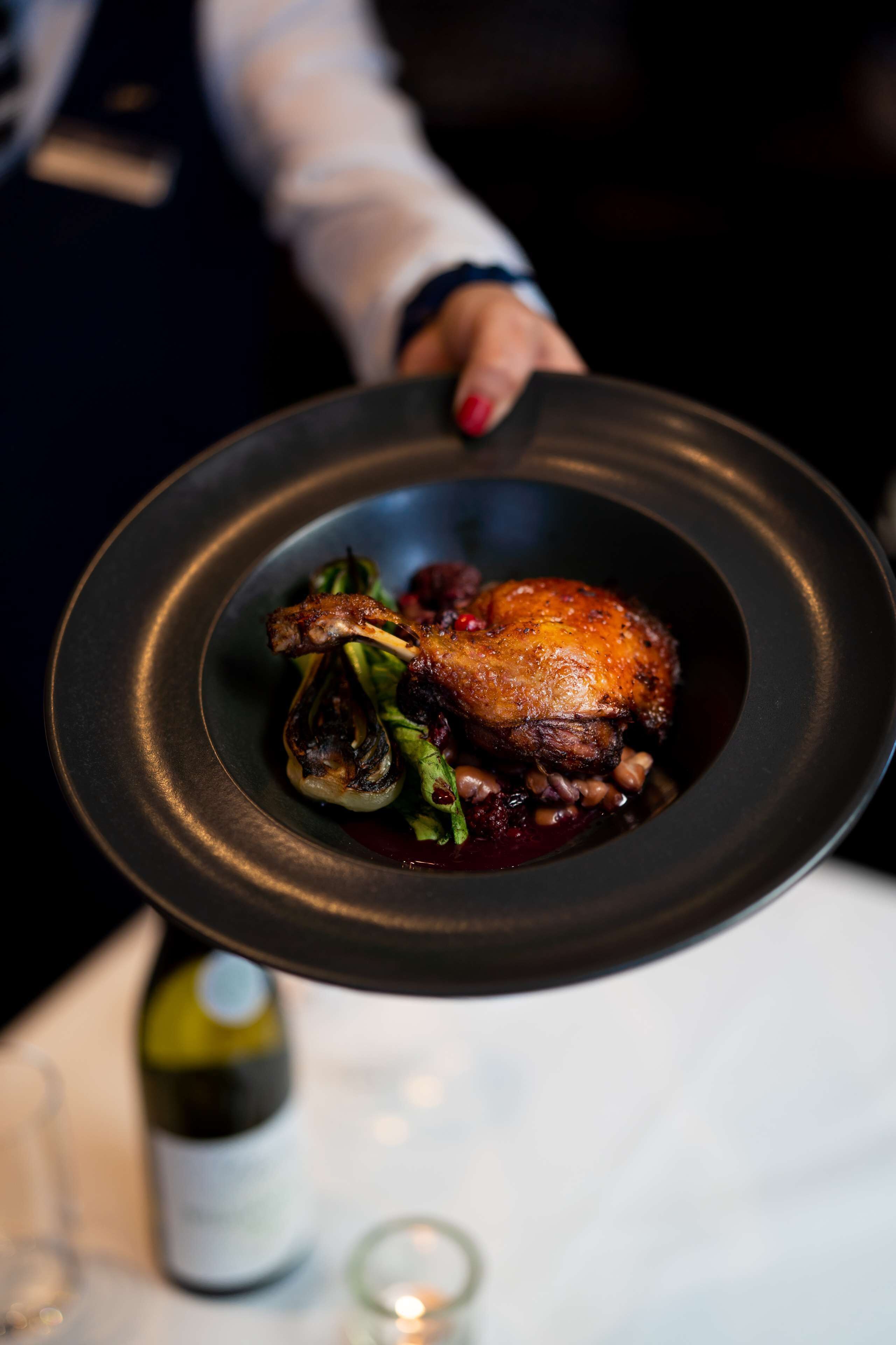 Une personne tenant une assiette noire sur laquelle se trouvent un poulet rôti et des légumes.