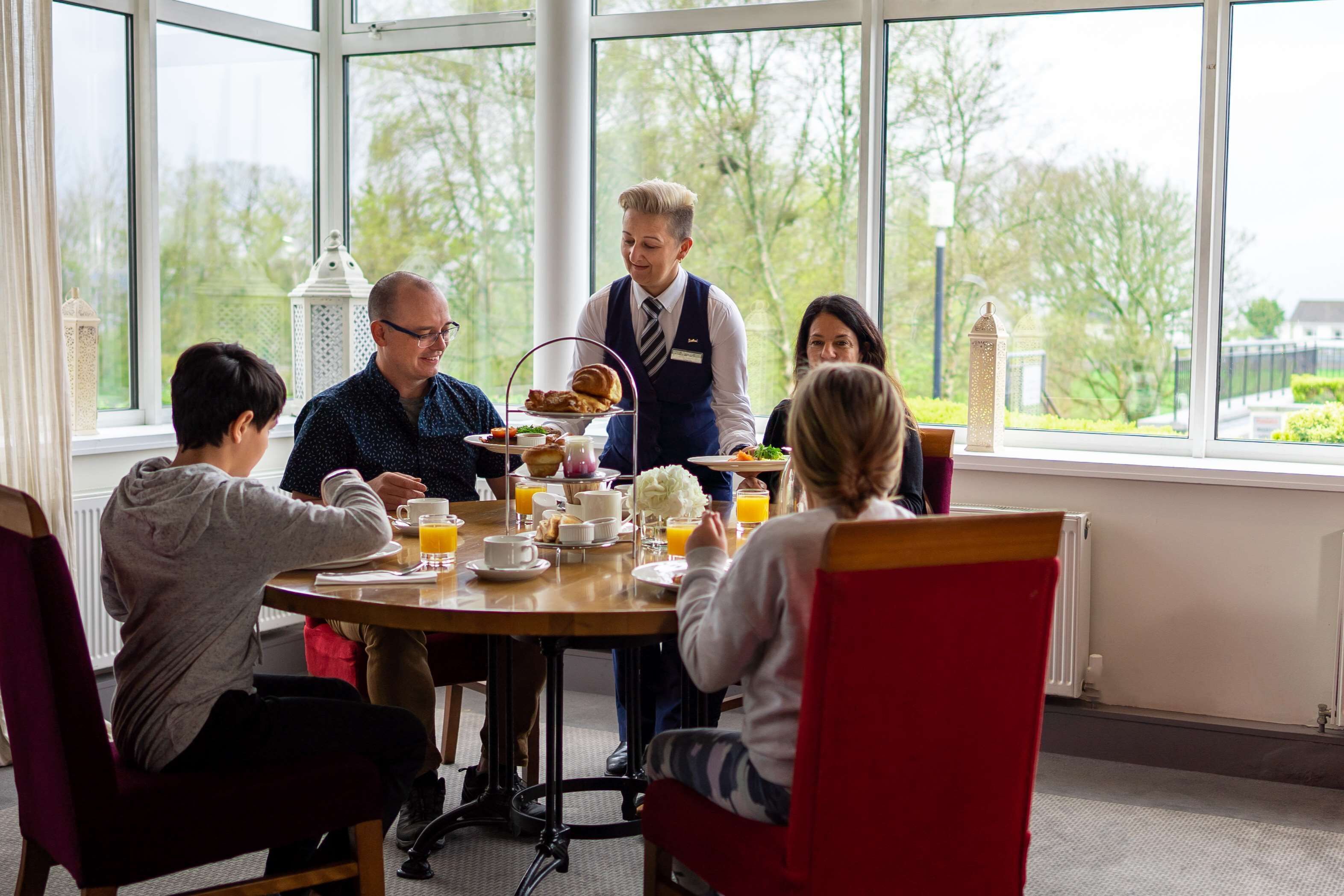 A breakfast setting with a table, chairs, and a waiter serving food.