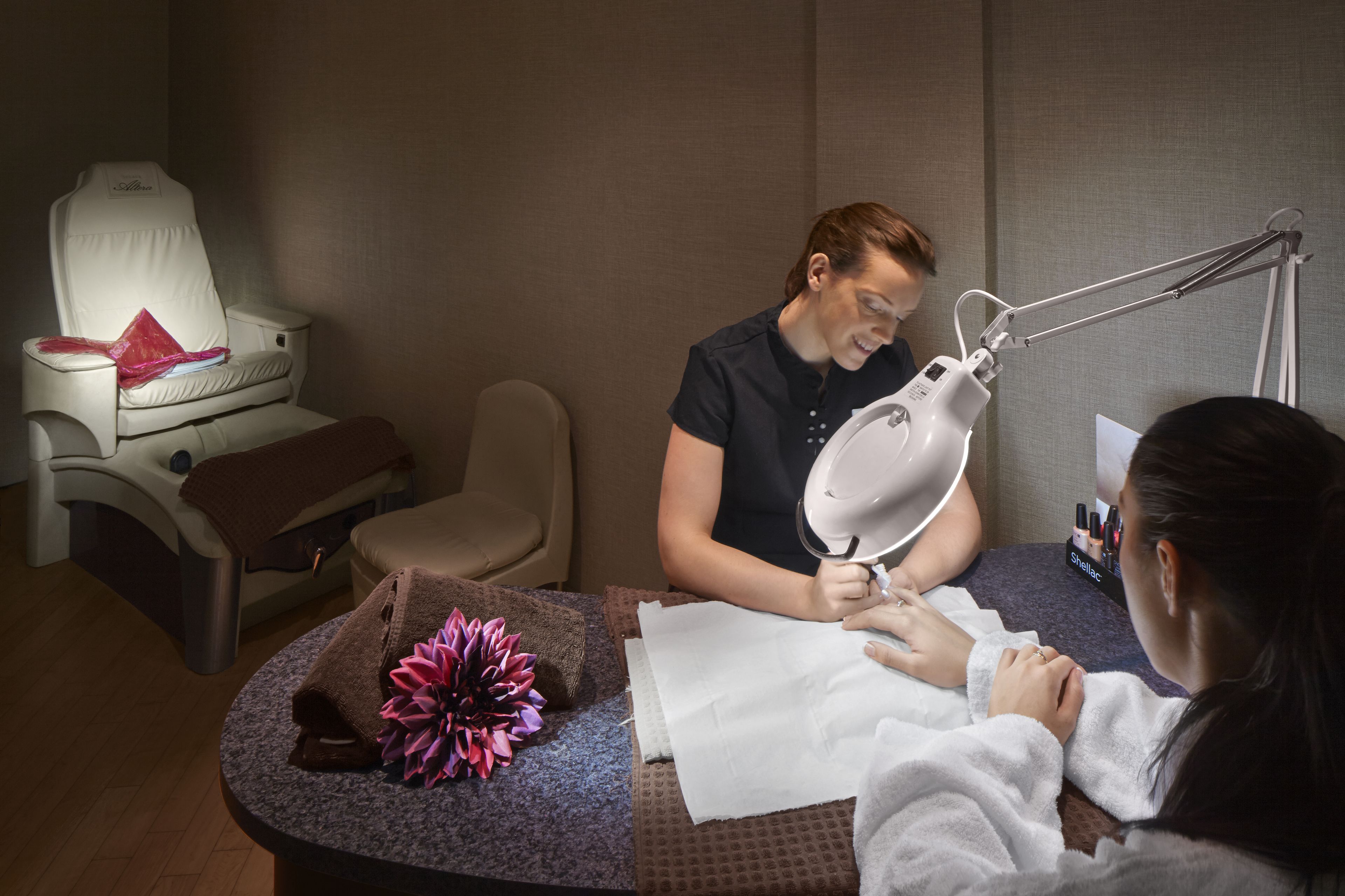 A nail salon with a massage chair, a mirror, and a tray with nail polish.