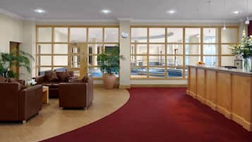 A spacious lobby with a red carpet, leather sofas, a reception desk, and large windows offering a view of a pool.