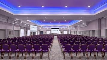 A conference room with rows of purple chairs and a large screen at the front.