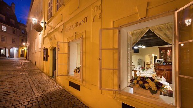 A hotel with a cobblestone street, open windows with curtains, and a flower arrangement visible through the window. - Boutique Hotel Constans (Prague)
