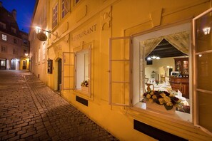A hotel with a cobblestone street, open windows with curtains, and a flower arrangement visible through the window. - Boutique Hotel Constans (Prague)