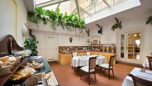 A dining area with tables set for breakfast, a buffet with various food items, and hanging plants. - Boutique Hotel Constans (Prague)