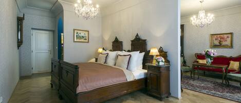 Un dormitorio con cama de madera, mesita de noche, cómoda, sofá rojo y una araña.