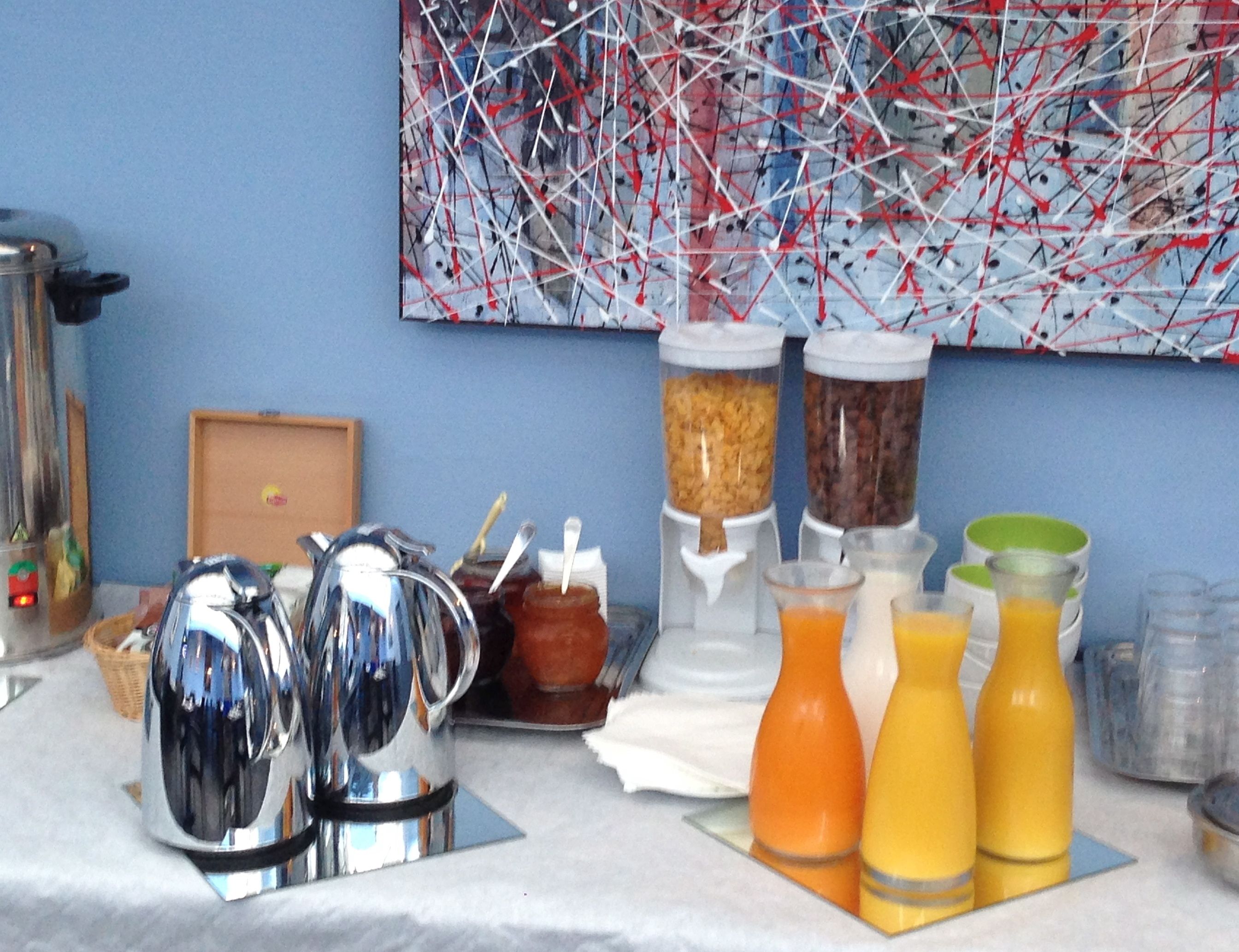 Una mesa con una cafetera, frascos de conservas y botellas de jugo de naranja.