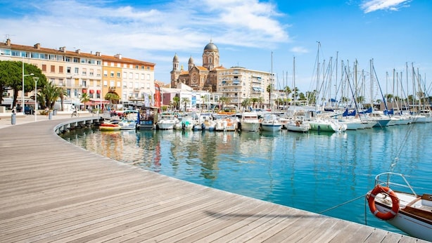 A marina with boats docked, a wooden boardwalk, and a prominent building with domes in the background. - Hotel de Flore (Saint-Raphael)