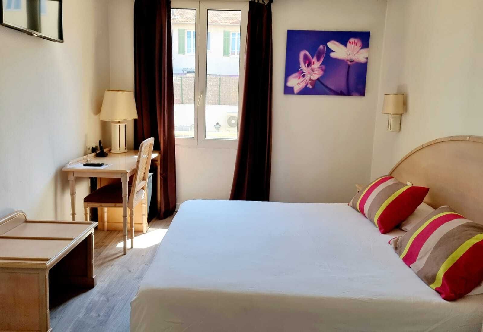 A hotel room with a bed, a desk, a chair, and a window with curtains.