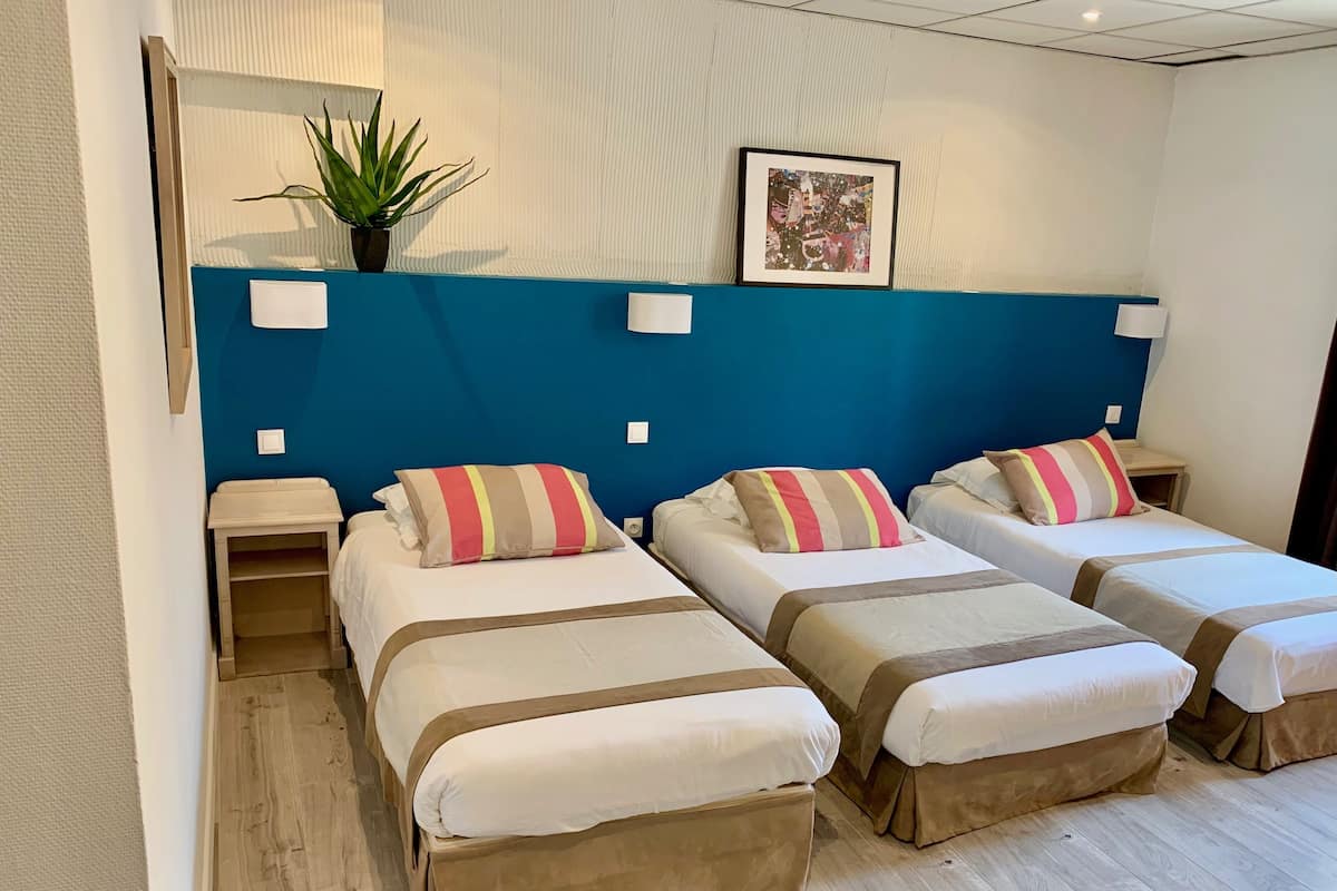 Habitación de hotel con dos camas, una pared azul decorativa, un cuadro enmarcado y una planta en maceta.