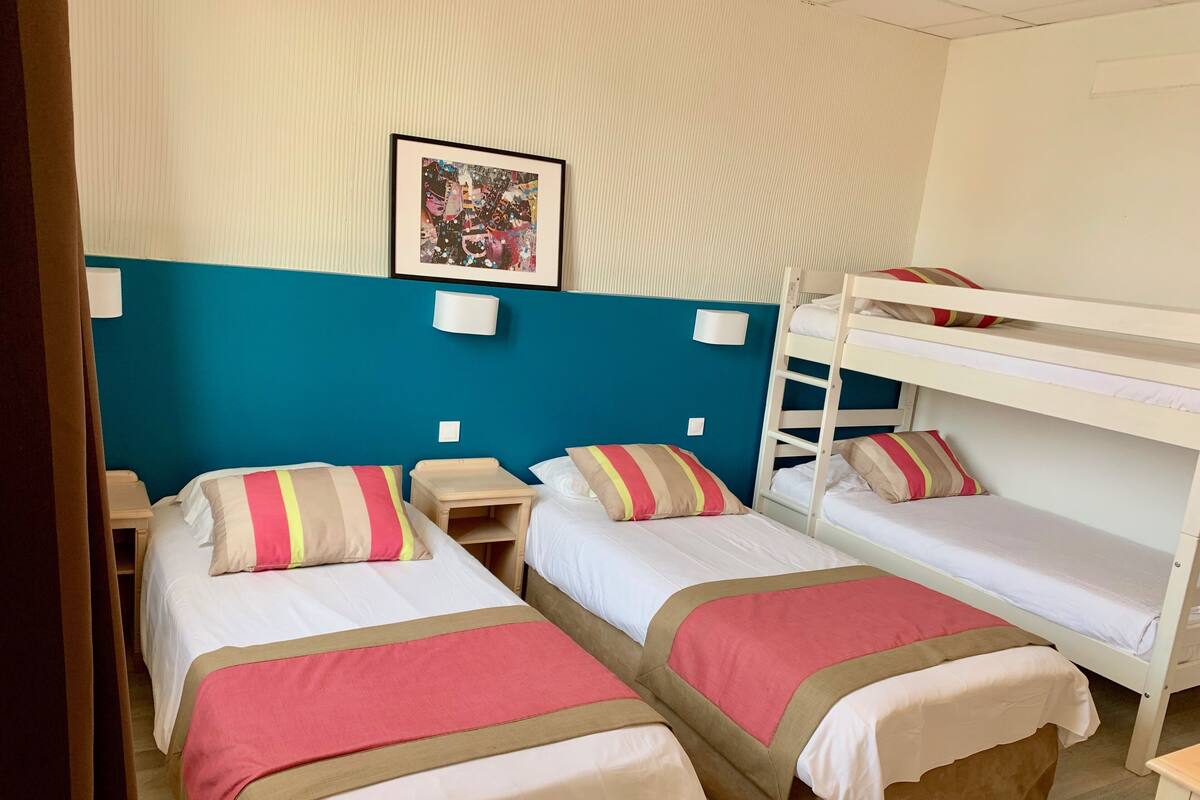Una habitación con dos camas individuales, una litera y una mesita de noche pequeña.