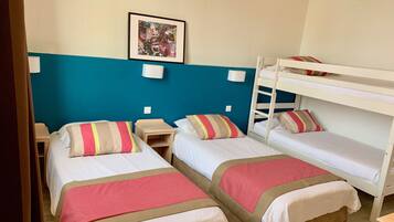 A room with two single beds, a bunk bed, and a small bedside table.