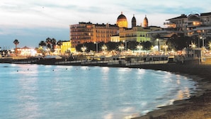 A waterfront hotel with a prominent dome and multiple towers, a promenade with street lamps, and a calm sea. - Hotel de Flore (Saint-Raphael)