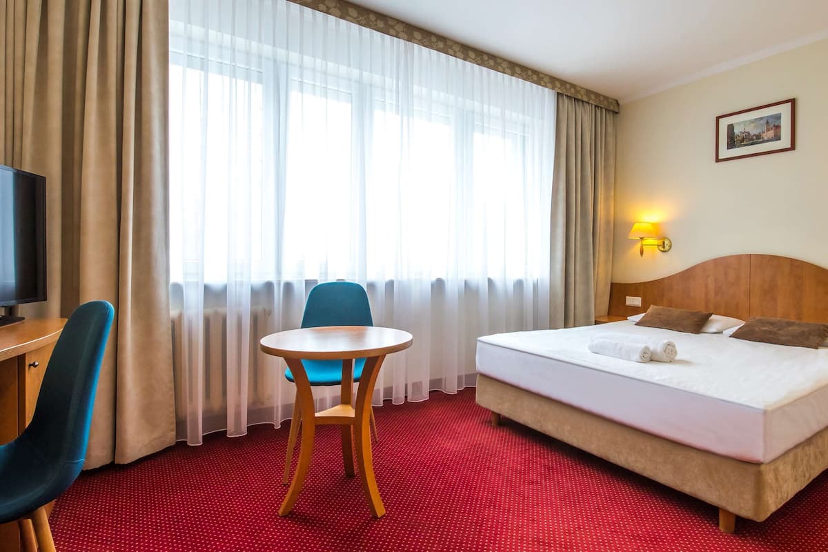 A hotel room with a bed, a desk with a chair, a small table, and two wall-mounted lamps.