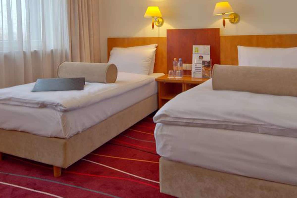 A hotel room with two beds, a red carpet, and a wooden headboard.