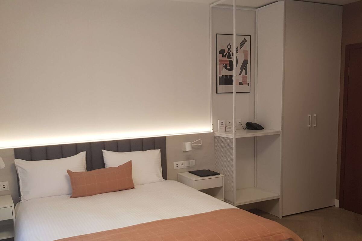 A neatly arranged bedroom with a bed, bedside tables, a wardrobe, and a framed picture on the wall.