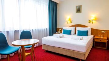 A hotel room with a bed, two chairs, a small table, a nightstand, and a window with curtains.