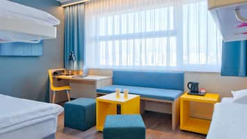 Une chambre d’hôtel moderne, équipée d’un lit, d’un bureau, d’un canapé bleu et d’une petite table avec une bouilloire.