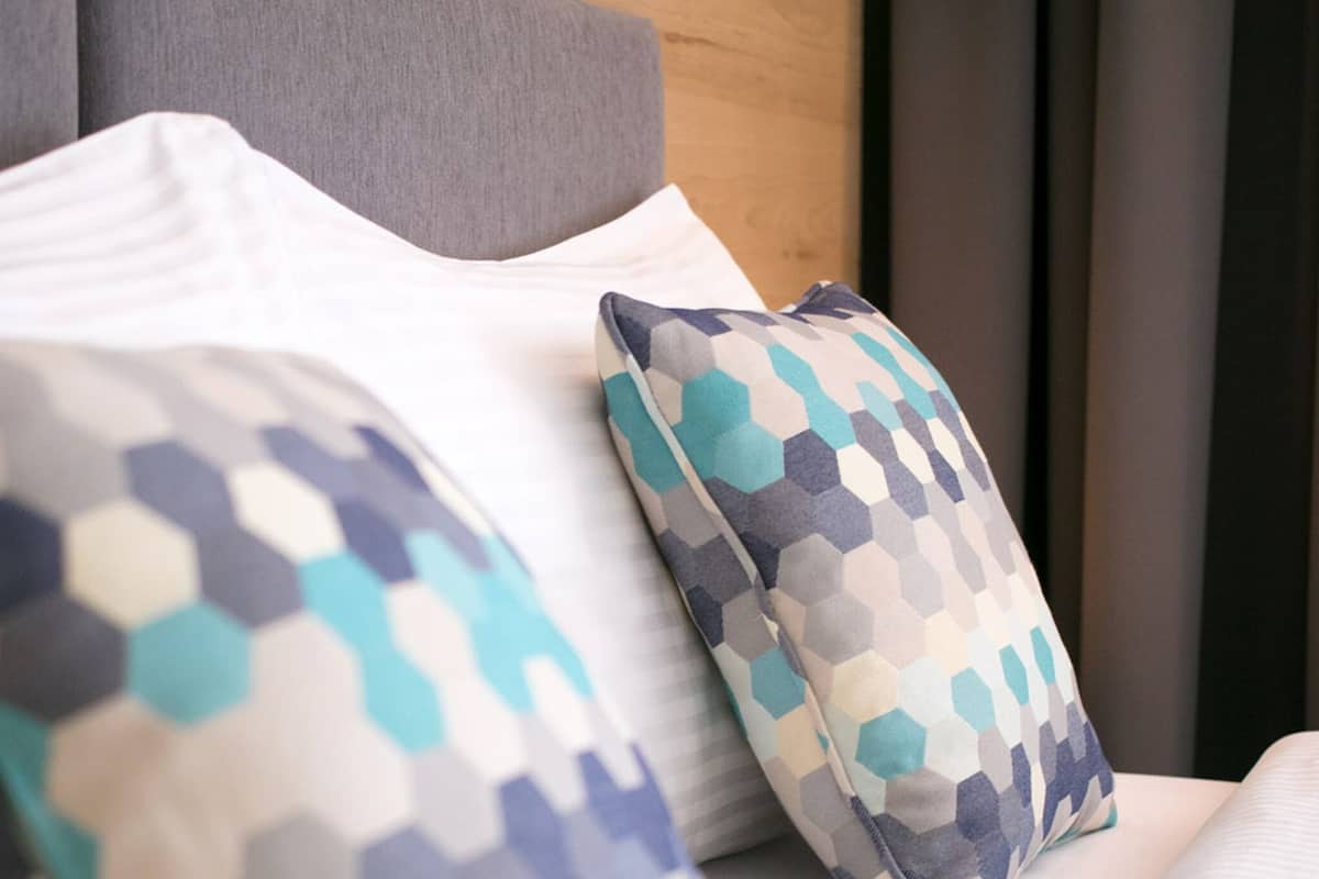 A bed with a white pillow and two patterned pillows with geometric designs.