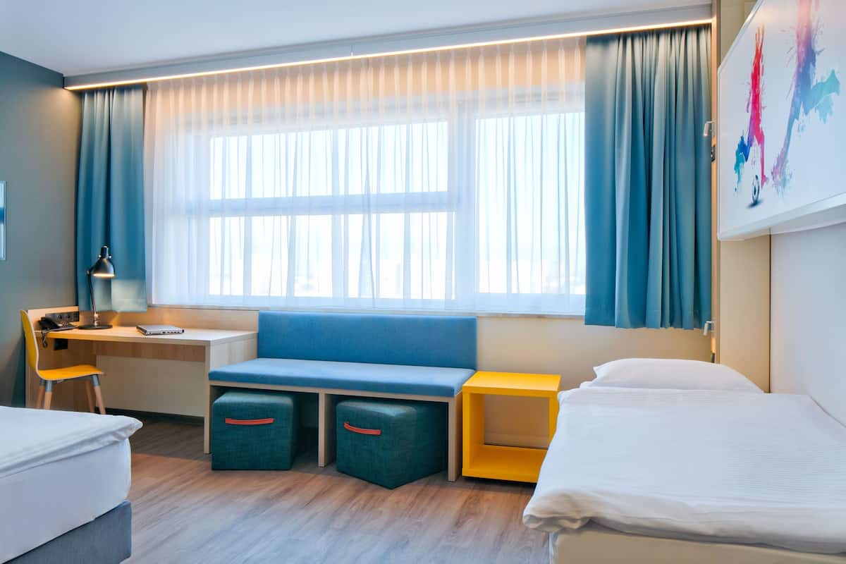 A hotel room with a bed, a desk, a bench, and a small table.