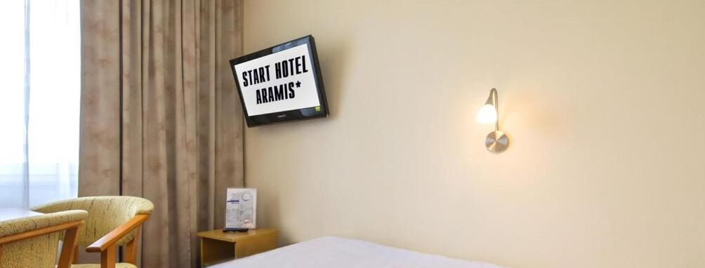 A hotel room with a bed, a chair, a nightstand, a sign reading "START HOTEL ARAMIS", and a wall-mounted light fixture.