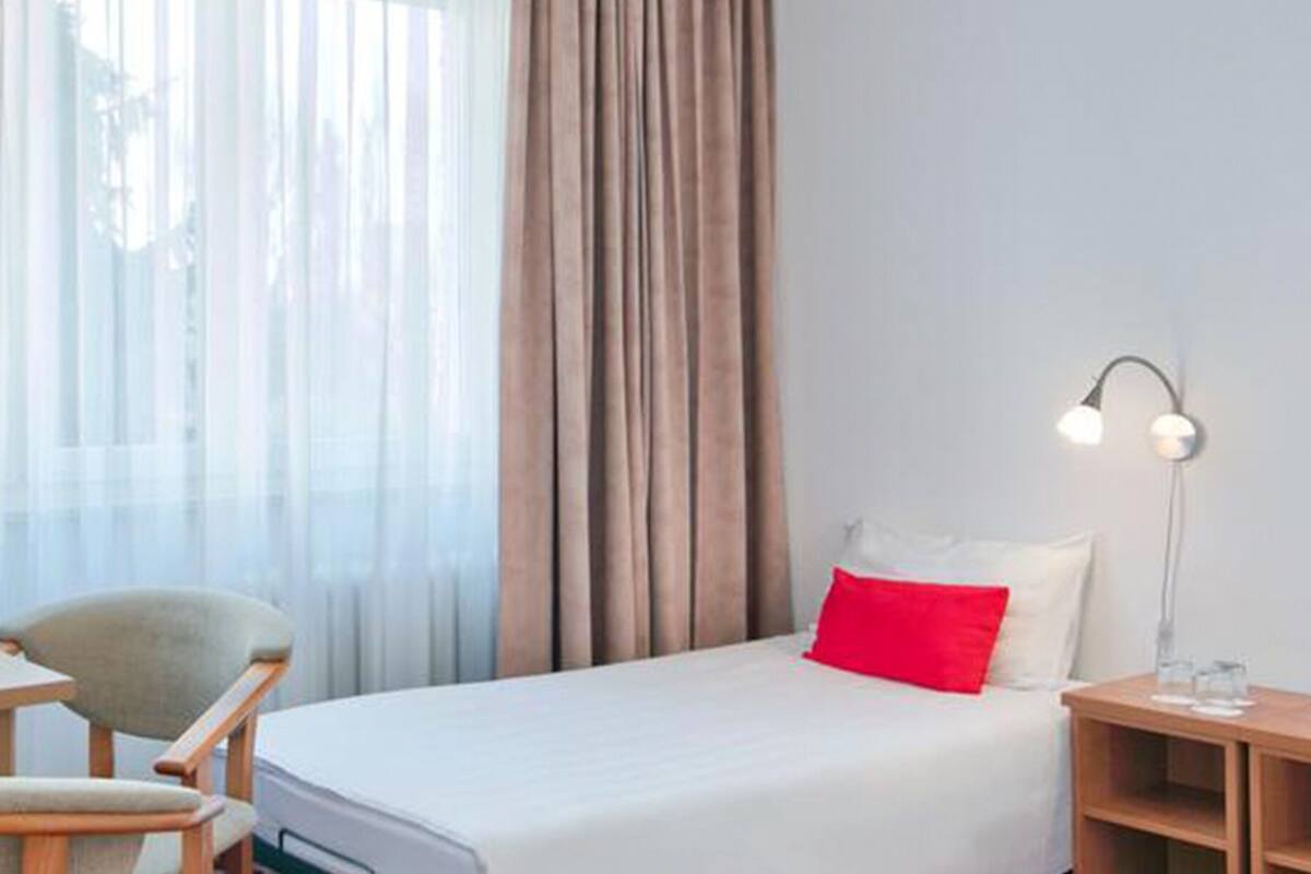 A hotel room with a bed, a desk, two chairs, a nightstand, and two wall-mounted lamps.