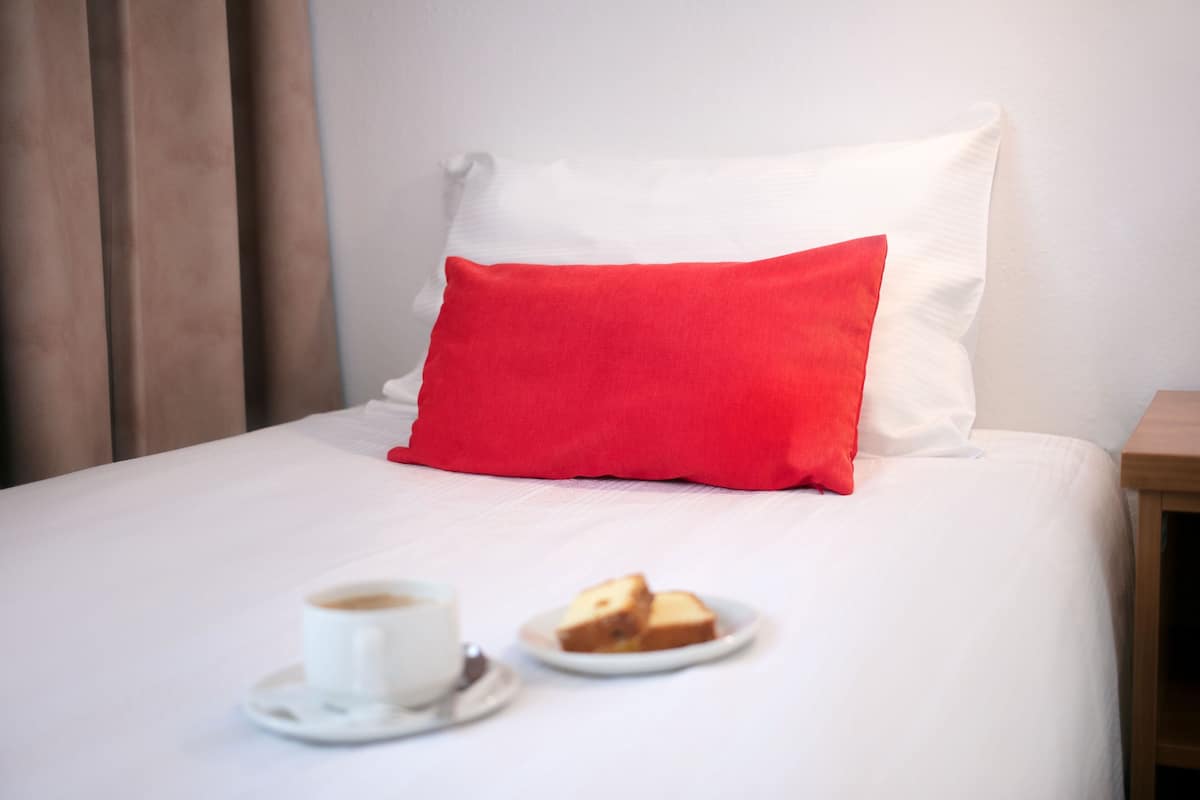 A neatly made bed with a white and red pillow, a cup of coffee, and a slice of toast on a plate.