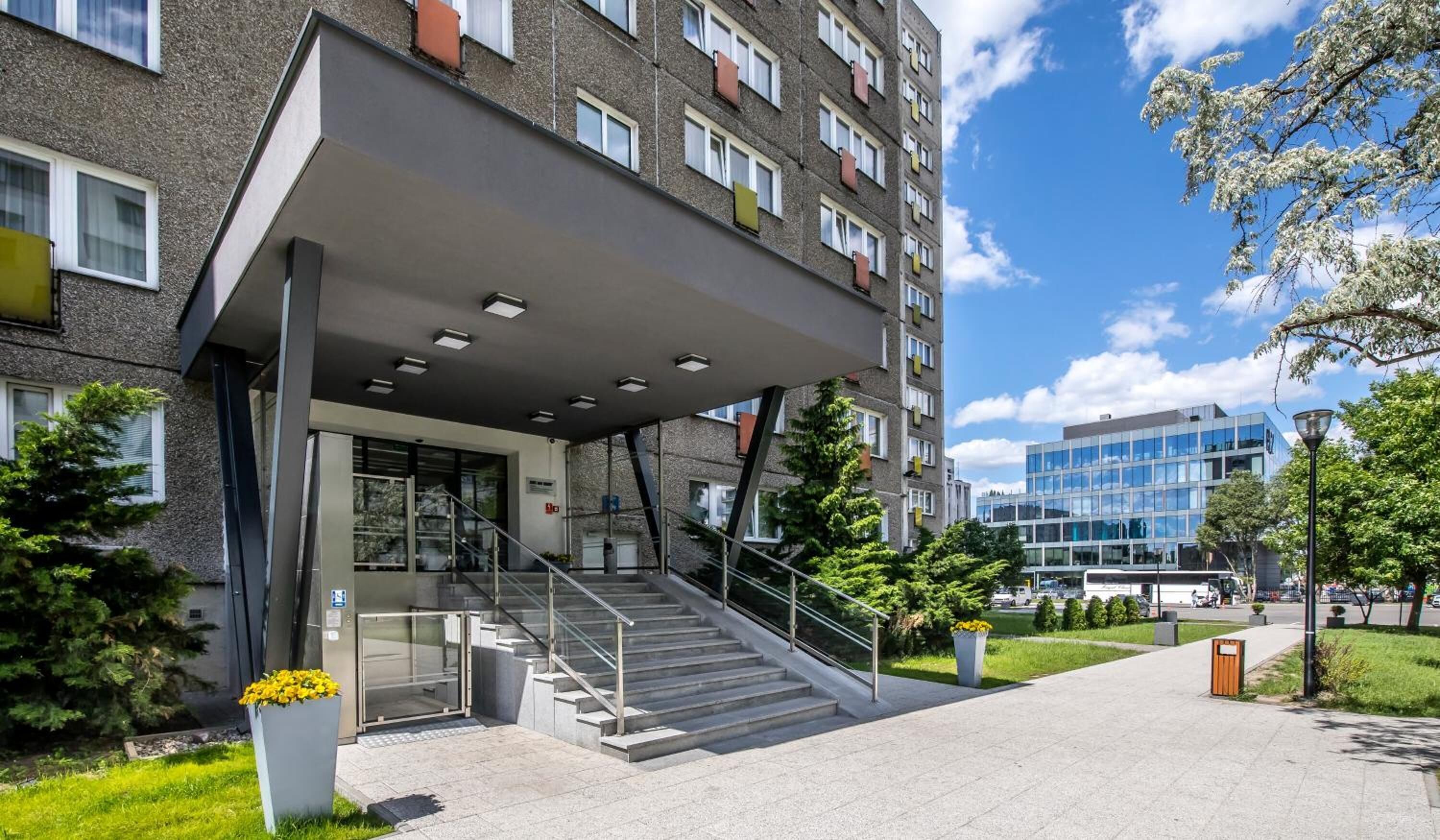 A modern building with a covered entrance, a staircase, and a glass facade in the background.
