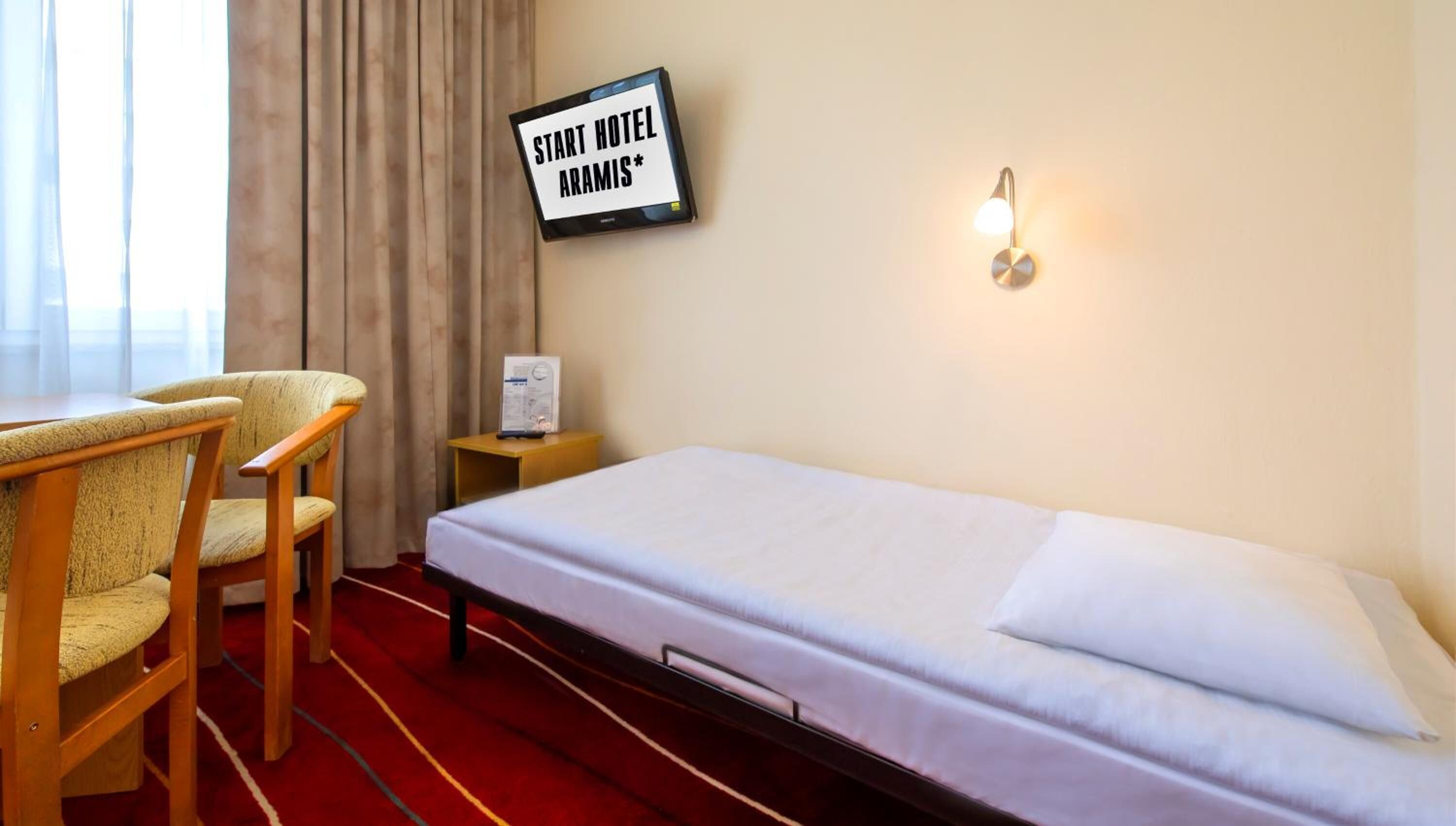 Ein Hotelzimmer mit Bett, Schreibtisch mit Stuhl, einem an der Wand befestigten Schild und einem Nachttisch mit Lampe.