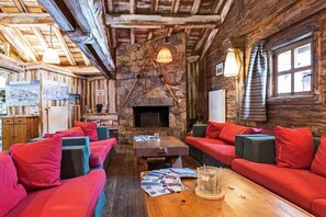 A cozy log cabin interior with a stone fireplace, wooden beams, and red upholstered seating. - Residence Lagrange Vacances le Village des Lapons (Hauteluce)