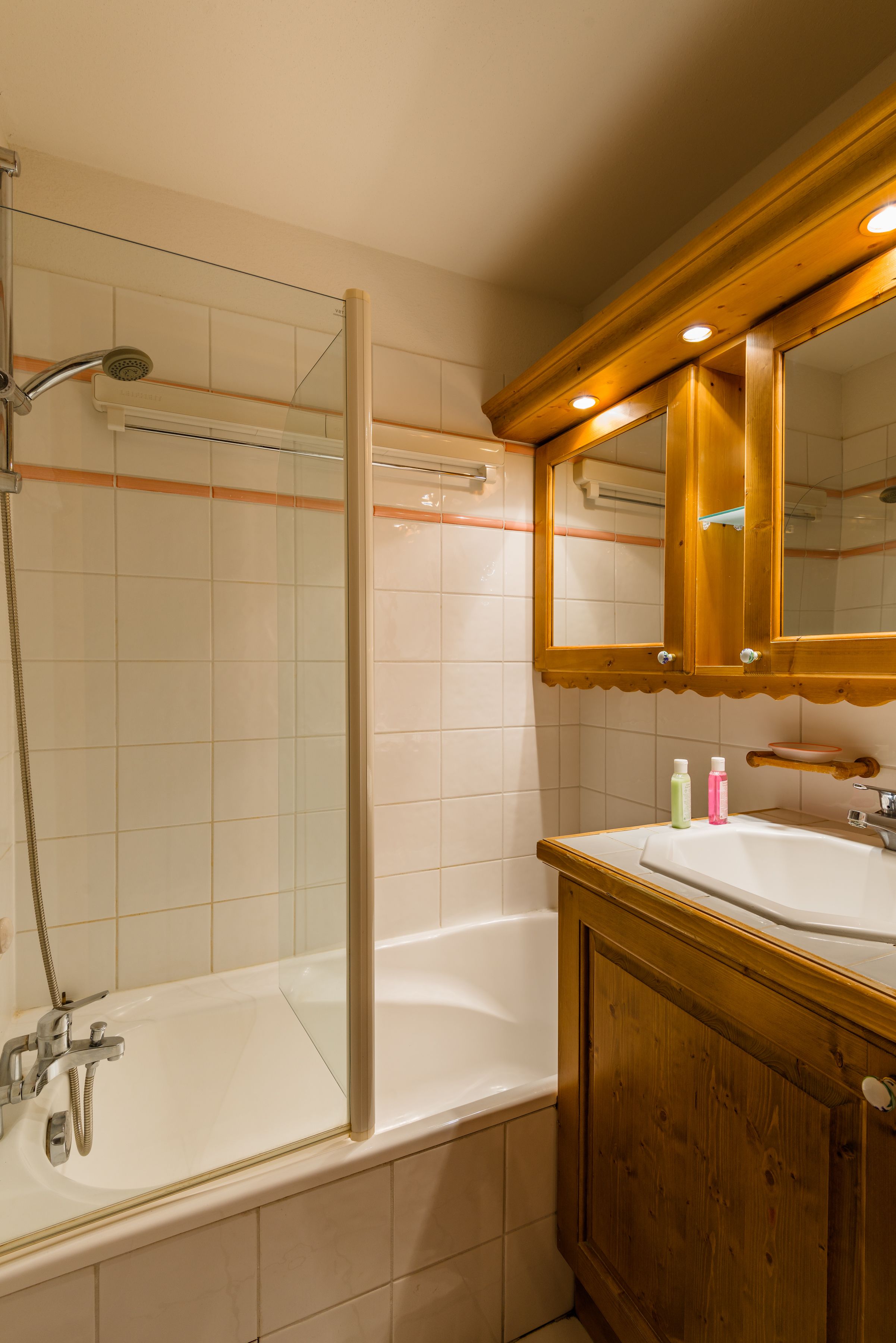 Un baño con ducha envuelta en vidrio, tocador de madera con espejo y bañera blanca.