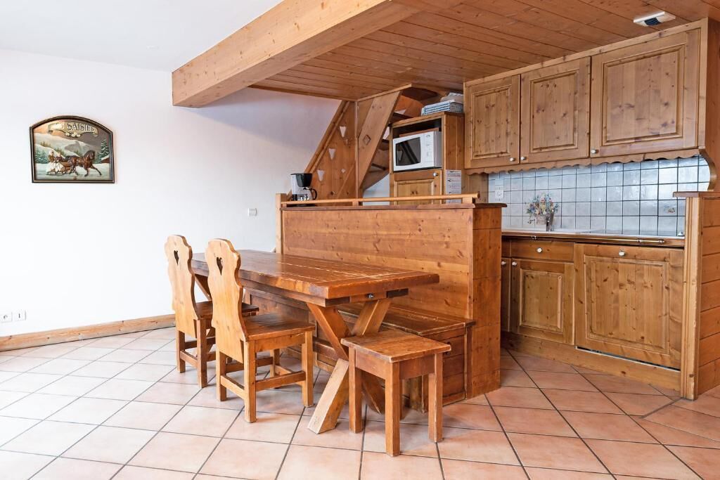 A wooden dining table with chairs, a kitchen with wooden cabinets, and a tiled backsplash.