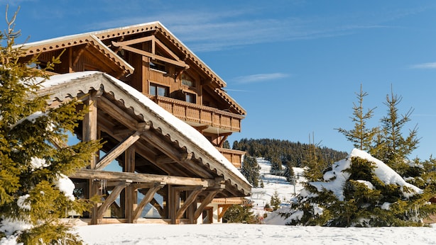 A wooden chalet with a balcony, surrounded by snow-covered trees and a clear blue sky. - Residence Lagrange Vacances le Village des Lapons (Hauteluce)
