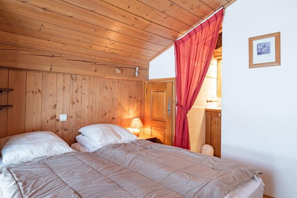 A wooden-paneled room with a bed, a nightstand, a lamp, and a door with a red curtain.