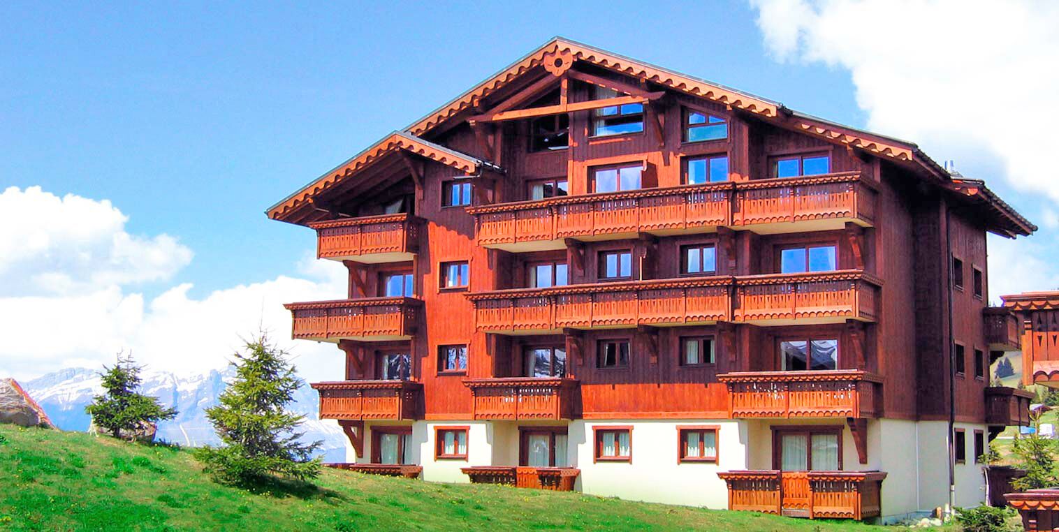 A multi-story wooden building with balconies, set against a mountainous backdrop.