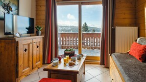 A cozy cabin with a wooden interior, a dining area with breakfast items, a television, and a view of a snowy landscape through the sliding glass doors. - Residence Lagrange Vacances le Village des Lapons (Hauteluce)