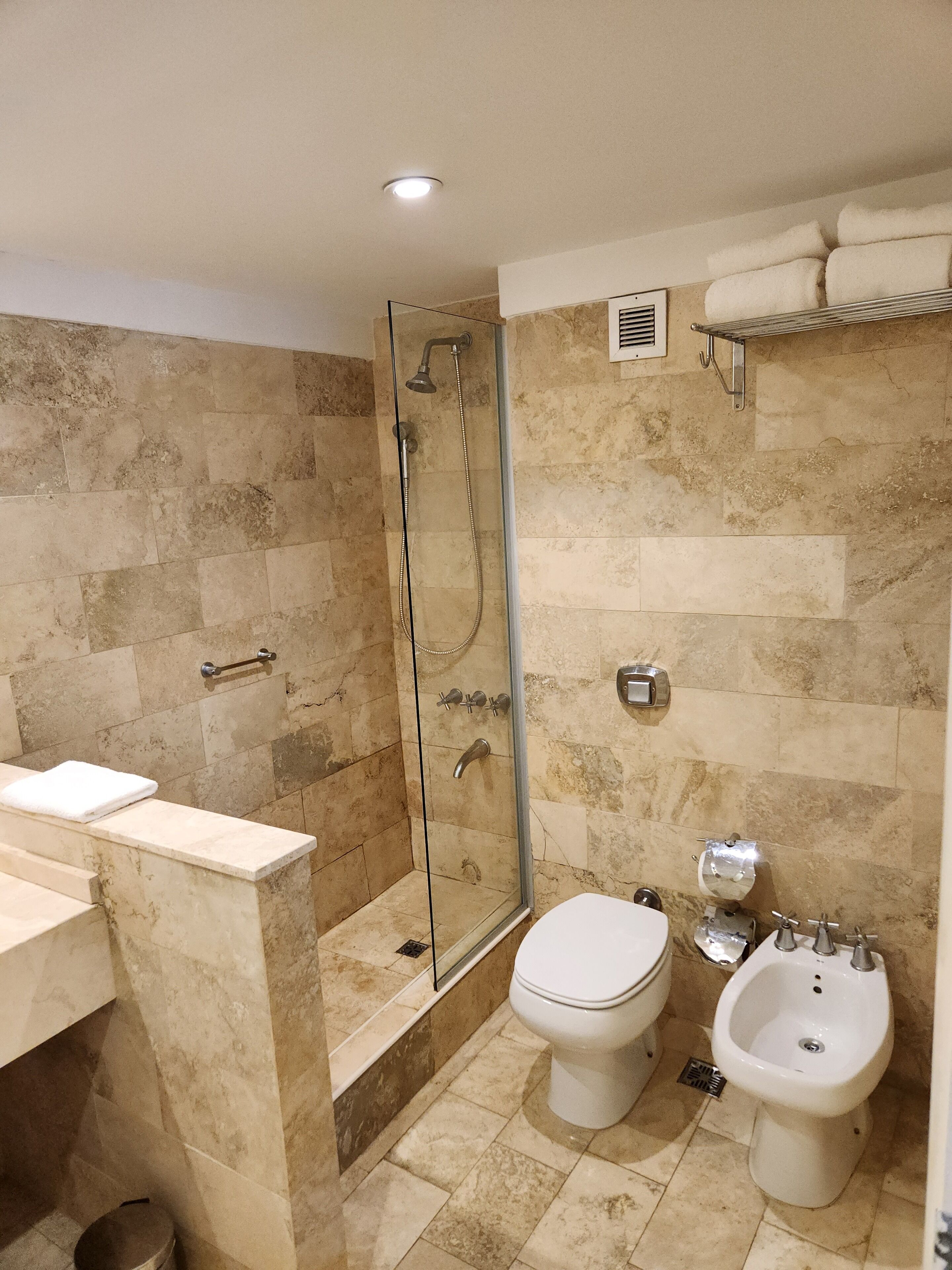 A modern bathroom with a glass-enclosed shower, a toilet, and a bidet.